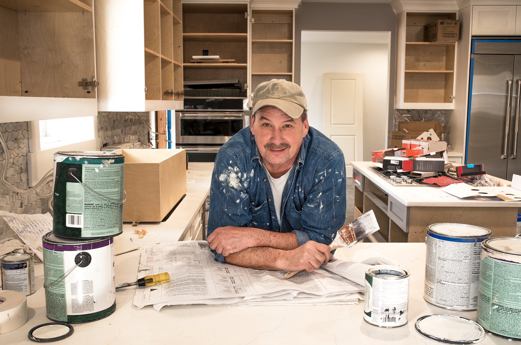 House painter in messy kitchen, with wet paint brush, looking at camera, in fixer upper house